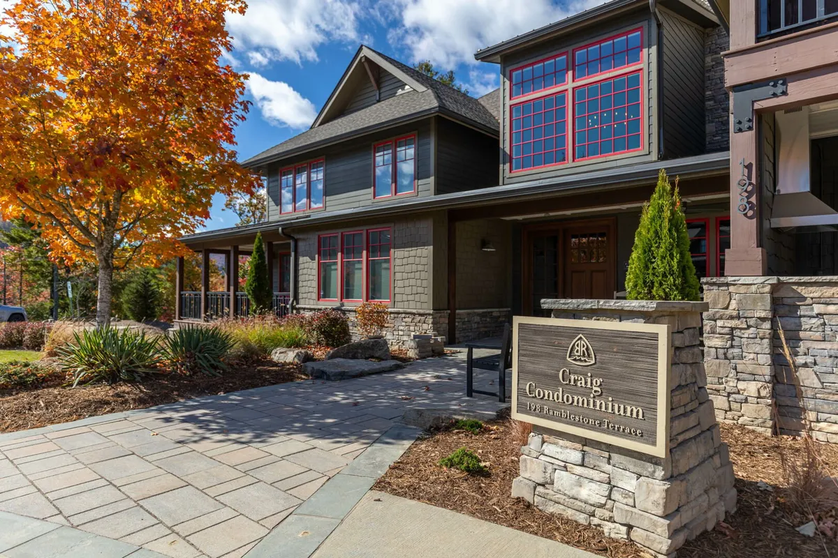 The image features the stone sign for the Blue Ridge Mountain Club surrounded by vibrant autumn foliage, with the condo building’s architectural details visible behind. The scene feels cozy and inviting, highlighting the beauty of the season and the upscale, welcoming atmosphere of the community.