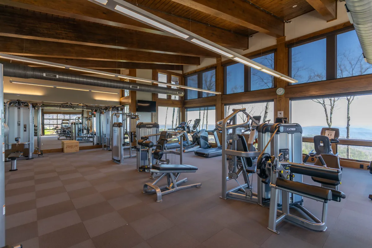 This image shows a spacious, well-equipped fitness center featuring exercise machines, large windows that let in abundant natural light, and wooden beams that add a touch of warmth to the modern space. The arrangement invites guests to work out individually or take part in group classes while enjoying mountain views through the windows.