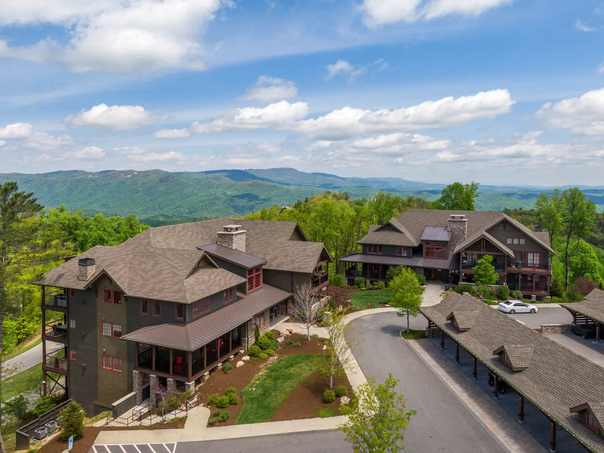 A panoramic view of a mountain range in the background, complemented by well-maintained gardens and striking architectural details of buildings. The overall mood is serene and peaceful, with a clear sense of connection to nature and resort living.