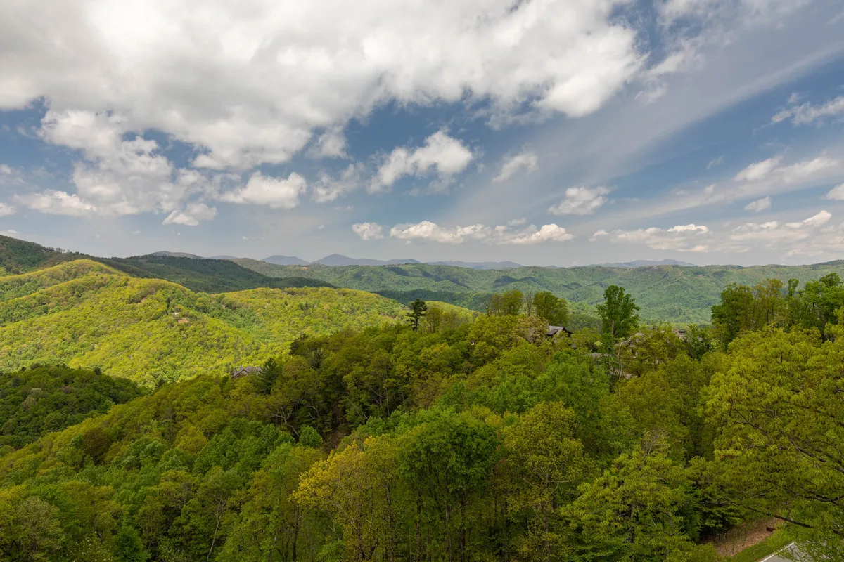 An expansive vista of rolling green hills, distant blue mountains, and an open, endless sky. The landscape is wild, unspoiled, and evocative of the outdoor experiences awaiting guests—perfect for those imagining days spent hiking, fishing, or simply exploring.