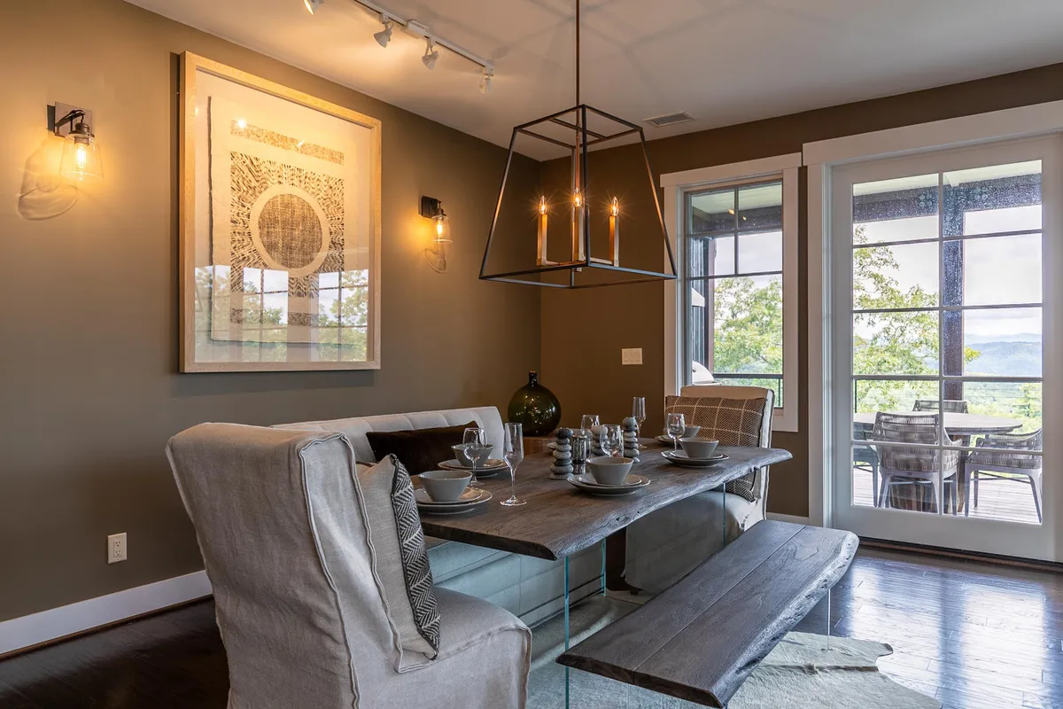 A warm dining area set with a large table, beautiful chandelier, and artwork on the wall. The space is bathed in natural light from windows that look out onto the mountain scenery, creating an inviting setting for meals and gatherings.