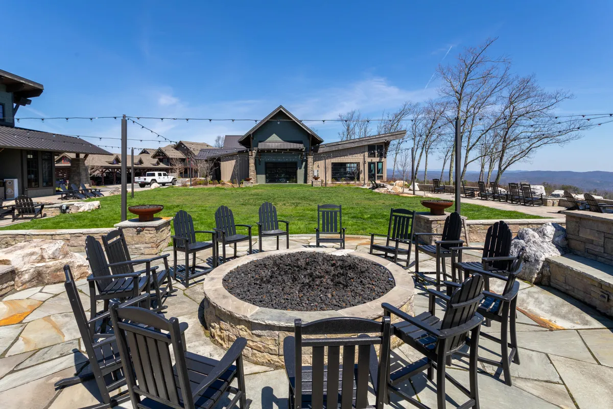An inviting fire pit area is surrounded by comfortable chairs on a well-groomed lawn, with distant mountains providing a breathtaking backdrop. The space is ideal for socializing, relaxing after a productive day, or stargazing in the evening.