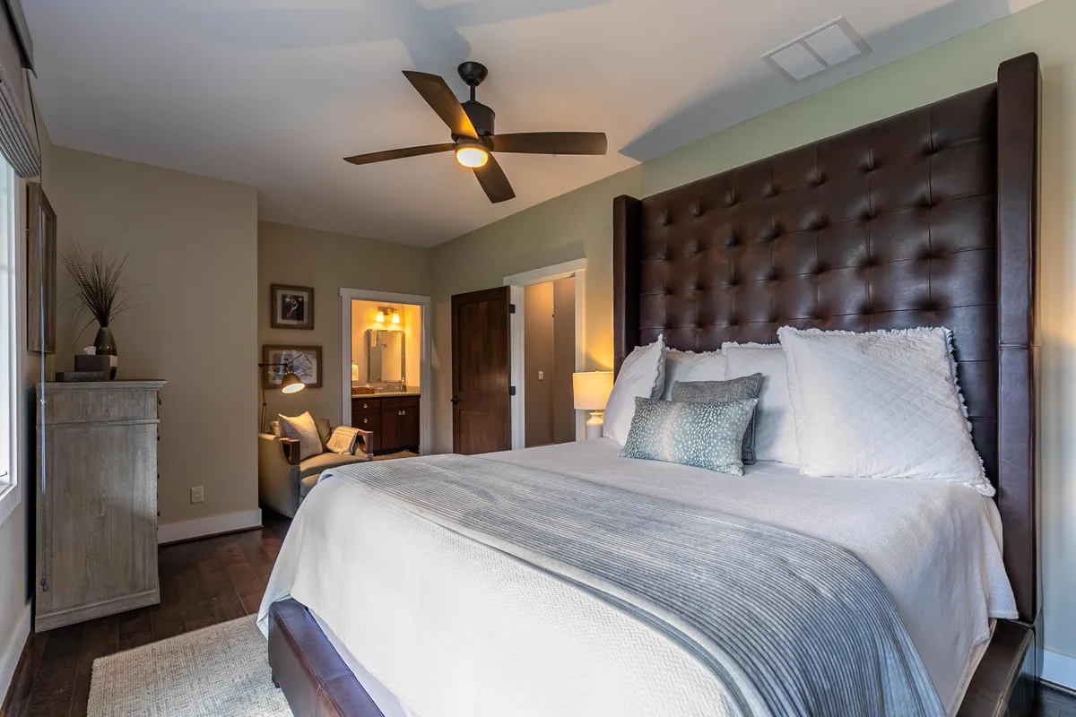 A cozy bedroom with a tufted headboard, decorative pillows, and a ceiling fan. The room is inviting and designed for relaxation, perfect for unwinding after a day of adventure or reflection.
