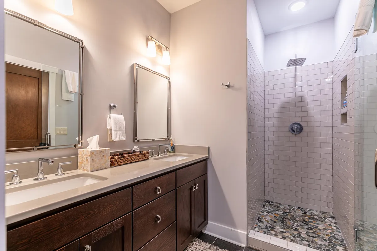 A modern bathroom with a double sink vanity, framed mirrors, and a spacious shower area. The space is inviting and calming, with updated fixtures and plush linens visible.