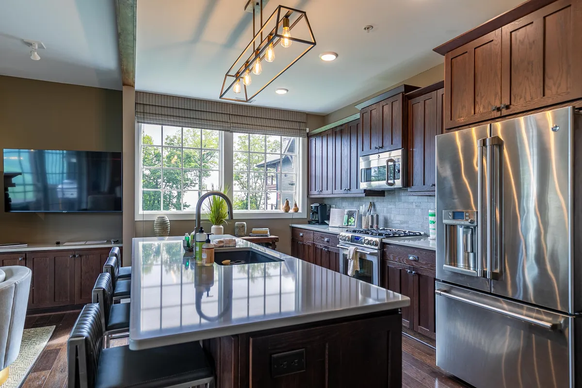A spacious chef’s kitchen with a large island featuring granite countertops, modern stainless steel appliances, ample cabinetry, and expansive windows that let in natural light. The layout is open and inviting, perfect for meal prepping or hosting guests.
