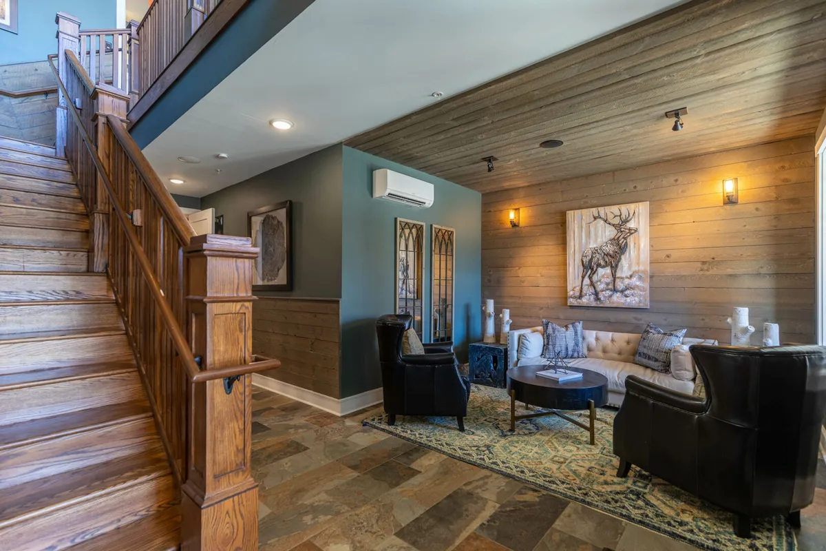 A ground-level entry area with a staircase to one side, cozy seating with chairs and a coffee table, and wildlife-themed artwork on the wall. The layout is accessible and inviting, providing a true sense of arrival and immediate comfort.