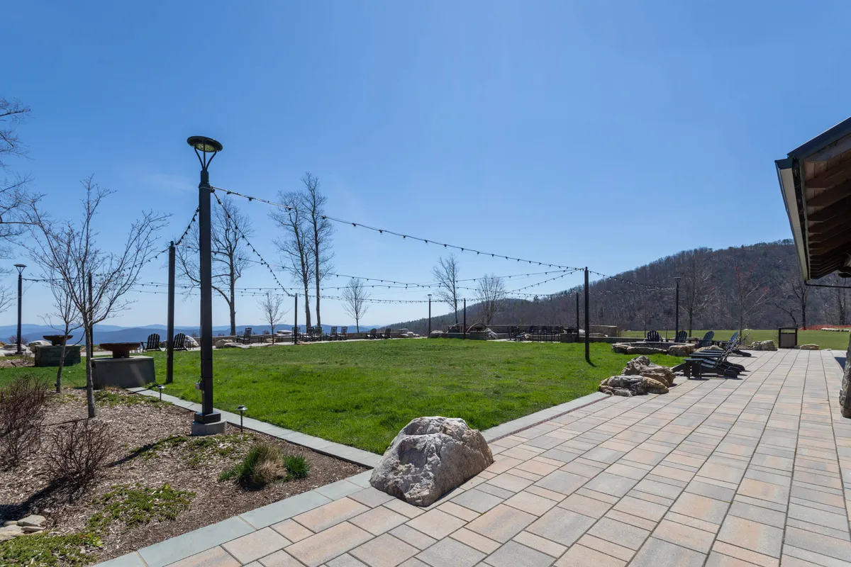 An outdoor grassy area is strung with twinkling lights and overlooks sweeping mountain views. Stone pathways meander through the space, and a fire pit invites relaxed outdoor gatherings, echoing the setting described for curated events, live music, and intimate evenings.